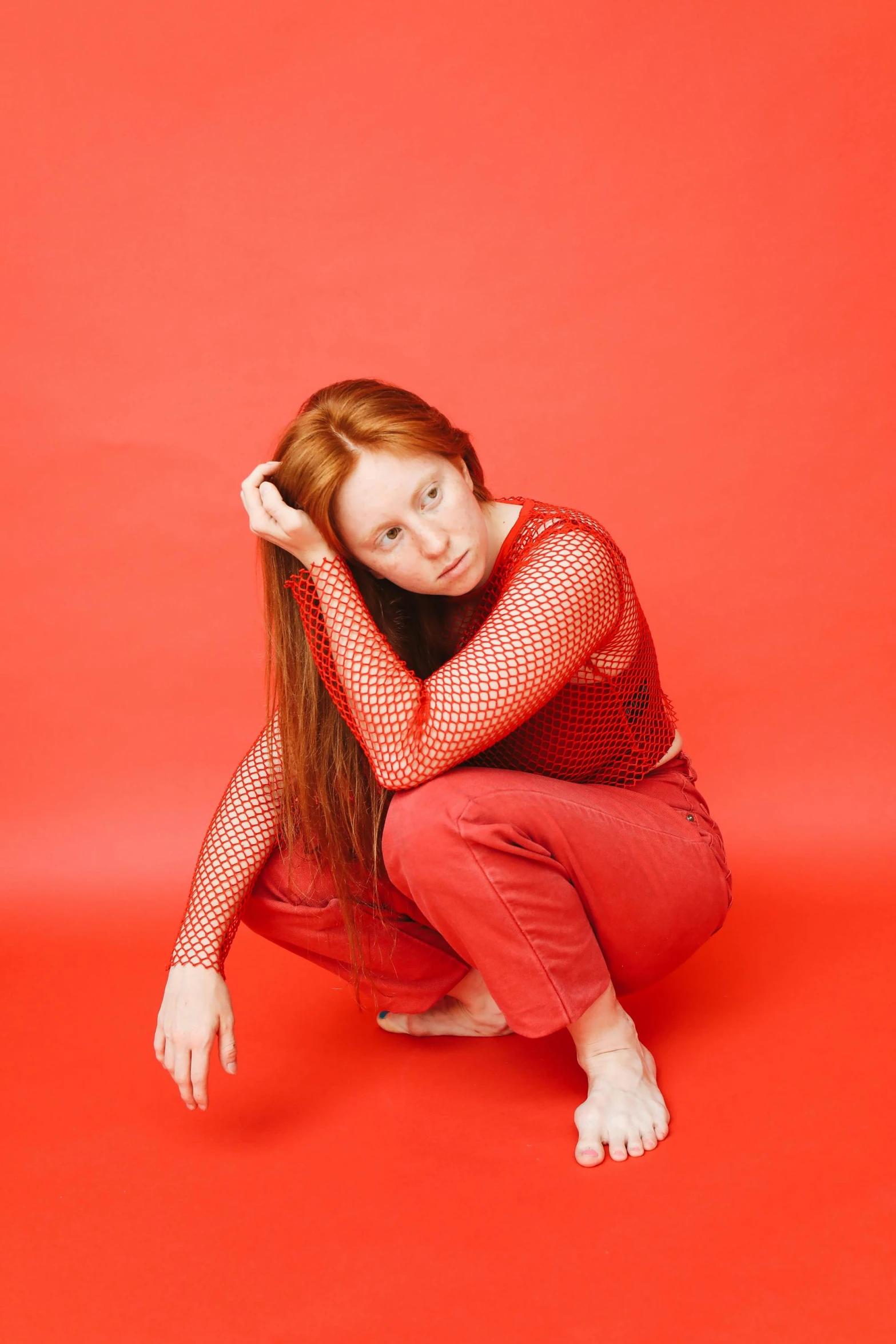 a woman sitting on top of a red floor, an album cover, by Isabel Naftel, trending on pexels, renaissance, ginger hair with freckles, red mesh in the facede, in front of white back drop, wearing a red outfit