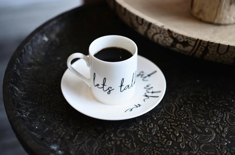 a cup of coffee sitting on top of a saucer, by Leila Faithfull, dau-al-set, penned with black on white, caligraphy, let's play, official product photo