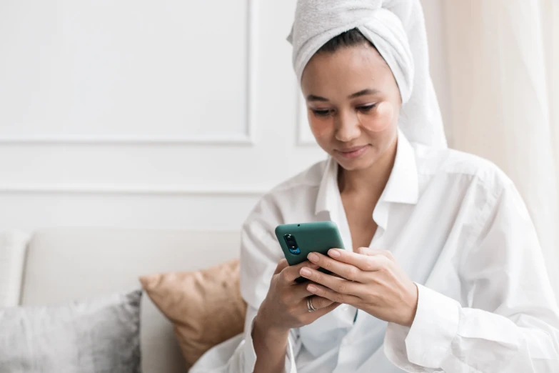 a woman with a towel wrapped around her head looking at her phone, trending on pexels, happening, wearing white silk robe, avatar image, thumbnail, skincare