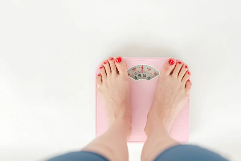 a woman standing on a scale with her feet on it, by Arabella Rankin, trending on pexels, square, pink, eating, steroid use