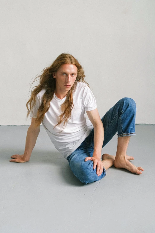 a woman sitting on the floor with her legs crossed, an album cover, by Lasar Segall, white shirt and blue jeans, ryan mcginley, long mane, man standing in defensive pose