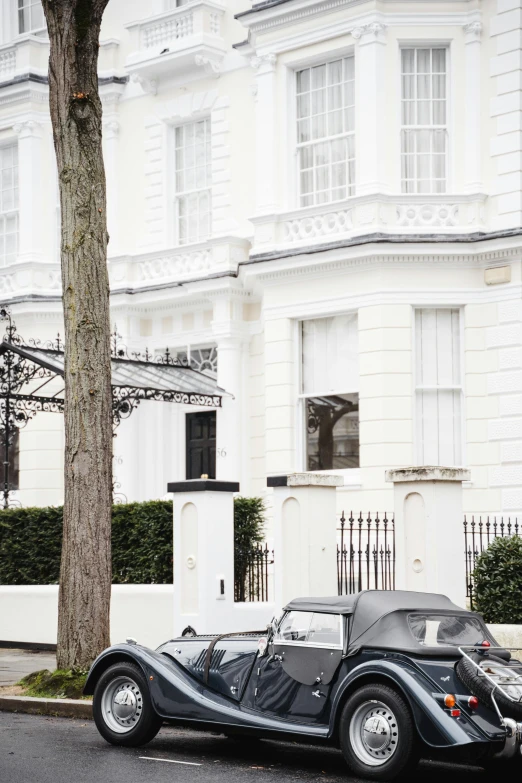 a vintage car parked in front of a white building, by Elsie Henderson, visual art, london cemetery, architectural digest, in front of the house, roadster