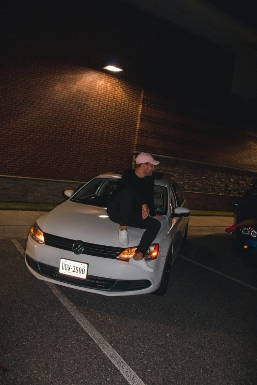 a man sitting on the hood of a white car, an album cover, unsplash, realism, low quality photo, at college, ((pink)), (((low light)))