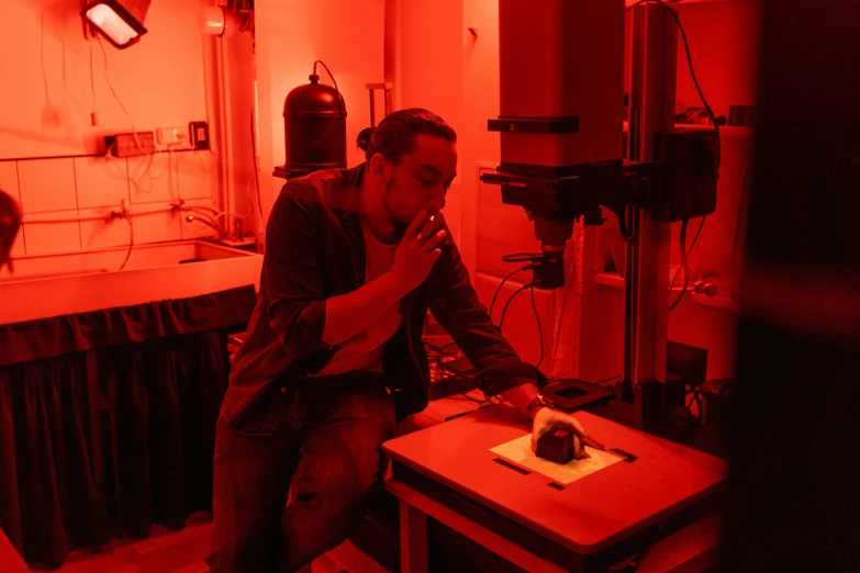 a man sitting on a chair in a room, red laser scanner, in a darkly lit laboratory room, plating, student