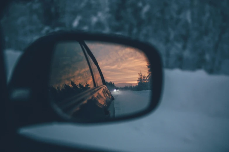 a rear view mirror of a car in the snow, inspired by Elsa Bleda, pexels contest winner, realism, cold sunset, looking from behind, mirror shades, holiday season