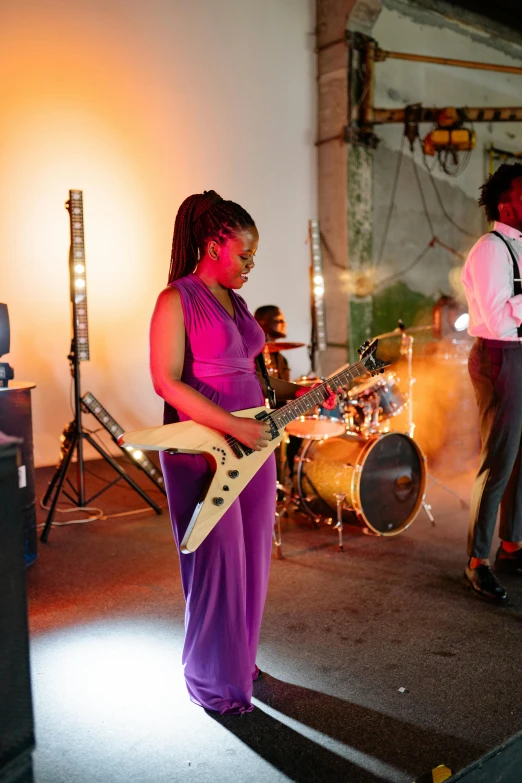 a woman in a purple dress playing a guitar, industrial party, african sybil, bassist, on set