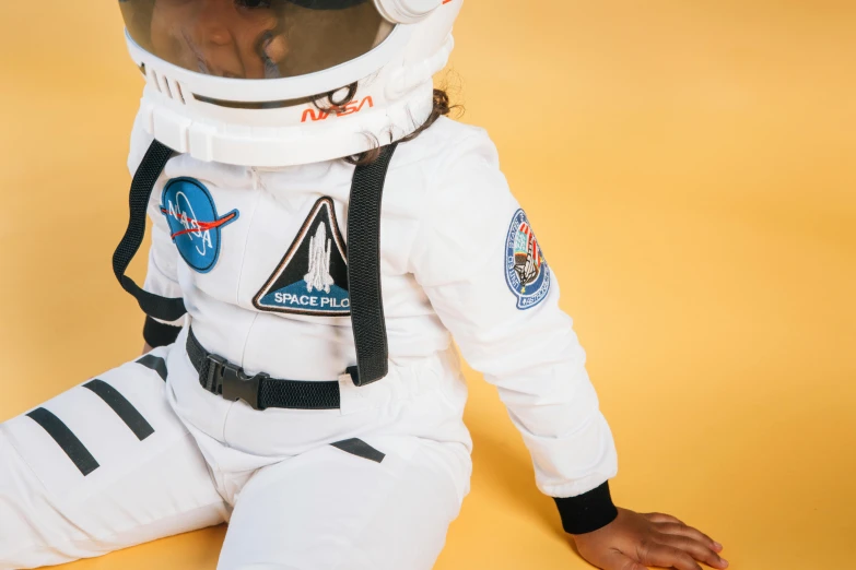 a child in a space suit sitting on the ground, trending on unsplash, afrofuturism, uniform off - white sky, ☁🌪🌙👩🏾, future inflatable jacket, apollo 11