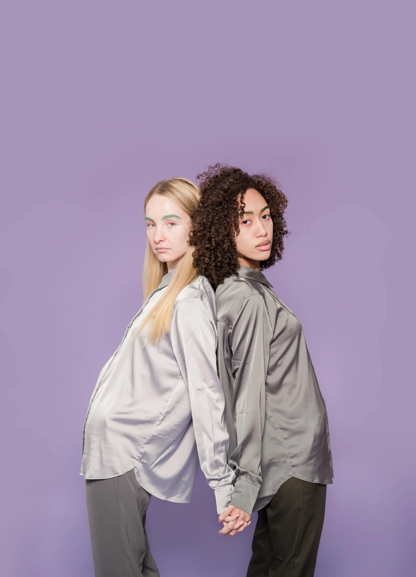 two women standing next to each other in front of a purple background, trending on pexels, antipodeans, gray shirt, performance, various posed, promotional image