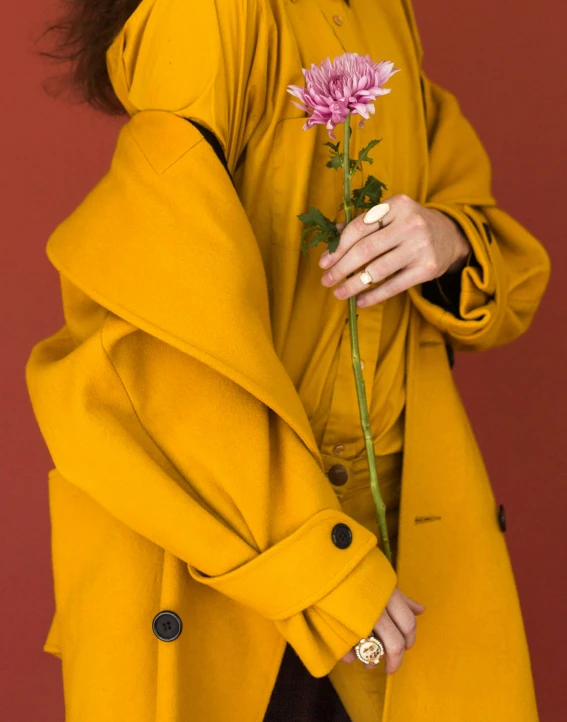 a woman in a yellow coat holding a flower, an album cover, trending on unsplash, non binary model, thumbnail, color image, outfit photo