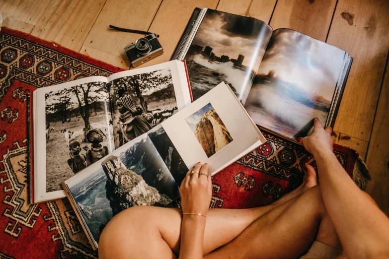 a woman sitting on a rug reading a book, a picture, pexels contest winner, art photography, old photobook, lots of pictures, on a wooden table, surf photography