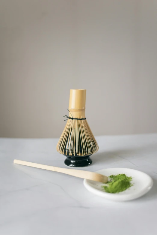 a whisk next to a plate of food on a table, inspired by Kanō Shōsenin, green tea, textured base ; product photos, black, bamboo