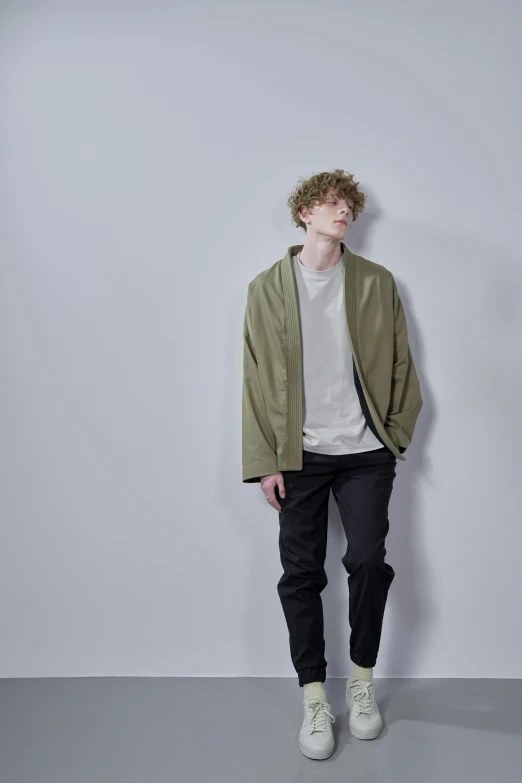 a man standing in front of a white wall, by Simon Gaon, wearing a haori, olive green, teenage boy, **cinematic