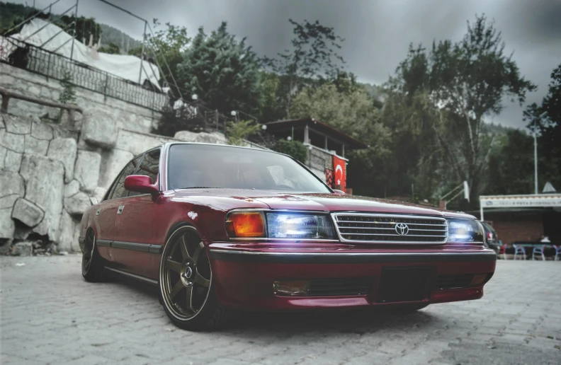a red car parked in front of a stone wall, a pastel, pexels contest winner, toyota jzx 1 0 0 drift, front lighting, ottoman sultan, 1 9 8 8