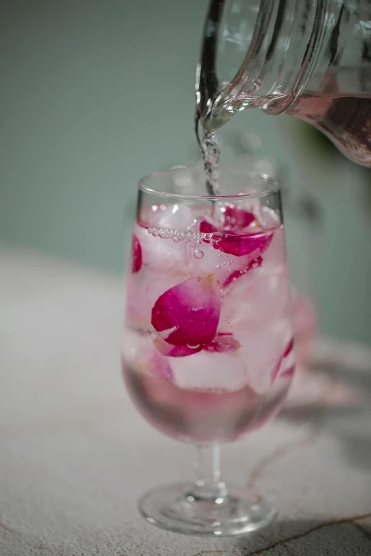 a person pouring water into a glass filled with ice, a still life, by Jessie Algie, unsplash, pink petals, made of drink, clean and pristine design, slide show