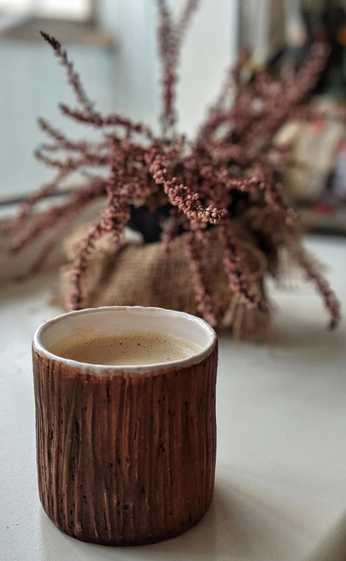 a cup of coffee sitting on top of a counter, by Jessie Algie, hurufiyya, textured base ; product photos, branches, made of bamboo, clay
