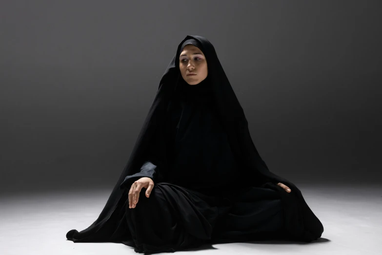 a woman in a black robe sitting on the floor, an album cover, inspired by Modest Urgell, hurufiyya, press shot, taken in the late 2010s, ninja, full view of face and body