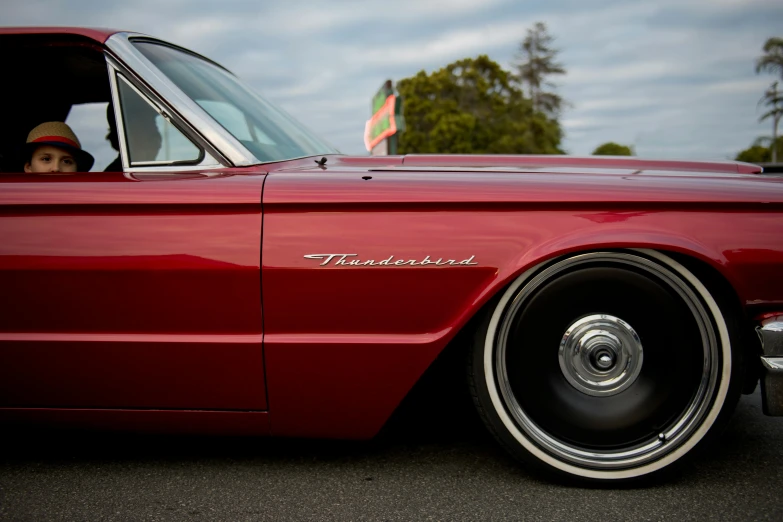 a man sitting in the driver's seat of a red car, trending on unsplash, photorealism, thunderbird 2, standing in front of lowrider, wine red trim, detailed alloy wheels