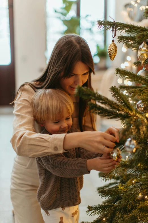 a woman and child decorating a christmas tree, profile image, grey, warmly lit, intimately holding close