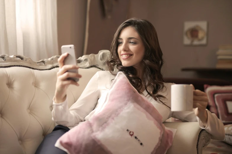 a woman sitting on a couch holding a cell phone, a picture, pixabay, happening, in love selfie, resting on a pillow, instagram post, with an elegant smile