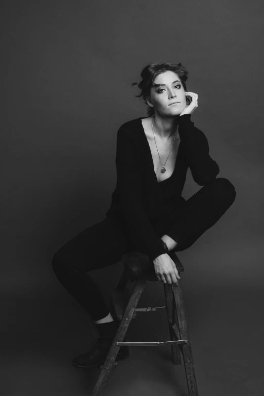 a black and white photo of a woman sitting on a stool, inspired by Peter Lindbergh, lucy hale, wearing a black catsuit, androgynous person, alison hannigan