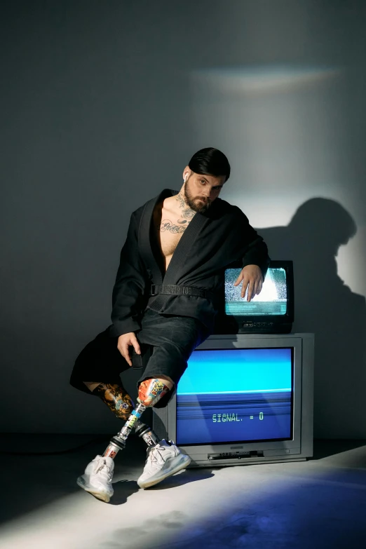 a man sitting on top of a table next to a tv, an album cover, inspired by Carlo Mense, massurrealism, robotic limbs on floor, zayn malik, showstudio, creative coder with a computer