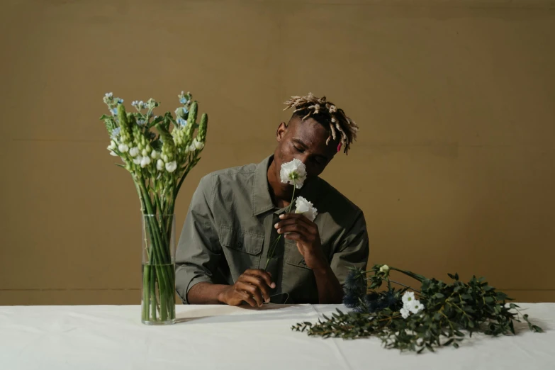 a man sitting at a table with flowers in front of him, an album cover, inspired by Barthélemy Menn, pexels contest winner, playboi carti portrait, simple aesthetic, holding flowers, side profile portrait