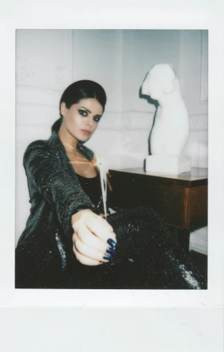 a woman sitting on top of a bed next to a lamp, a polaroid photo, kylie jenner as catwoman, showstudio, sleek hands, fujicolor photo