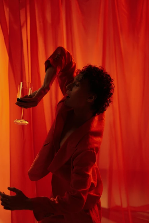 a woman in a red dress holding a glass of wine, an album cover, inspired by Carrie Mae Weems, magical realism, cai xukun, orange lighting, red curtain, lecherous pose