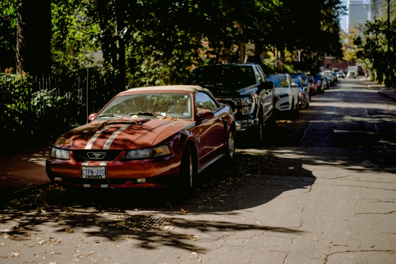 a red car parked on the side of a road, a tilt shift photo, by Carey Morris, pexels contest winner, photorealism, mustang, shady alleys, late 2000’s, lined up horizontally