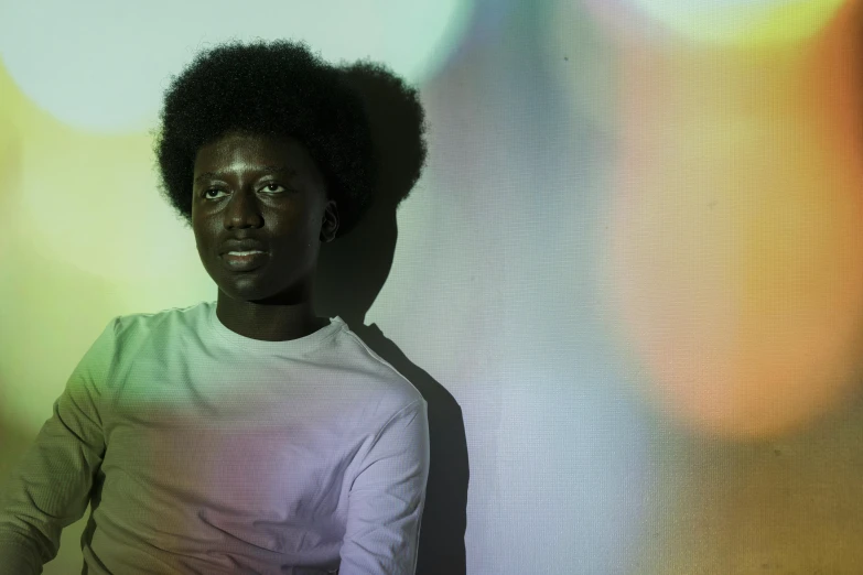 a close up of a person sitting in front of a wall, afrofuturism, soft volumetric lights, adut akech, light over boy, coloured photo