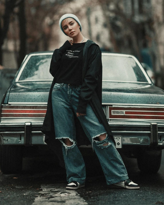 a woman standing in front of a parked car, an album cover, trending on pexels, wearing jeans and a black hoodie, style of julia razumova, promotional image, vintage clothing