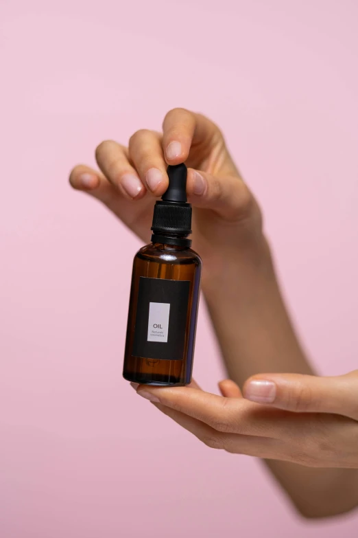 a woman holding a bottle of essential oil against a pink background, by Julia Pishtar, label, black oil, product view, 40 mm