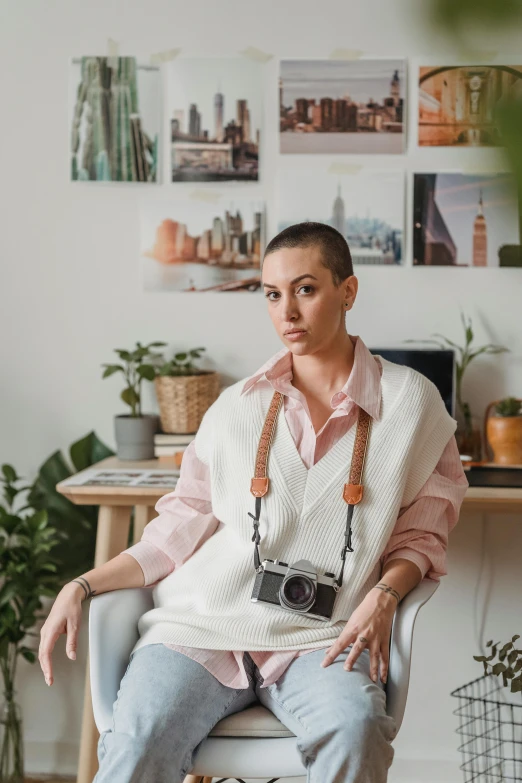 a woman sitting in a chair holding a camera, a portrait, inspired by Julia Pishtar, trending on pexels, wearing a white sweater, in office, non binary model, model is wearing techtical vest