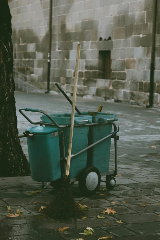 a blue cart sitting next to a tree on a sidewalk, by Elsa Bleda, pexels contest winner, broomstick, in barcelona, trash can, vintage photo