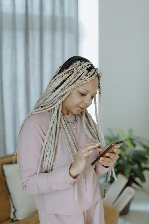 a woman standing in a living room using a cell phone, trending on pexels, renaissance, white braids, dreadlock breed hair, asian female, grayish