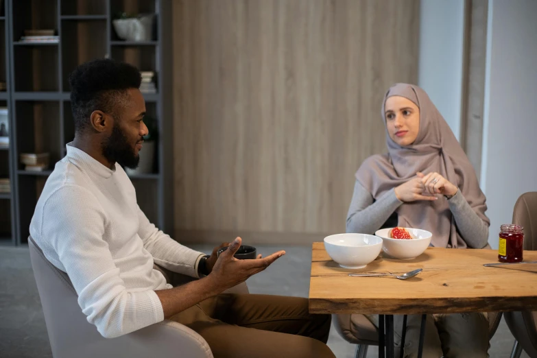 a man and a woman sitting at a table, by Washington Allston, pexels contest winner, hurufiyya, islamic, grey, talking, 😭🤮 💔