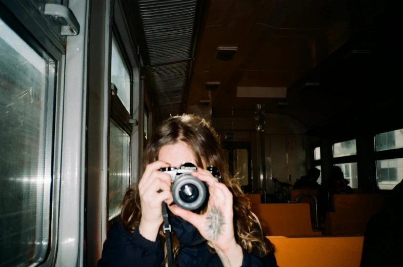 a woman taking a picture of herself with a camera, inspired by Elsa Bleda, photorealism, sat down in train aile, high-quality photo, photography], medium format