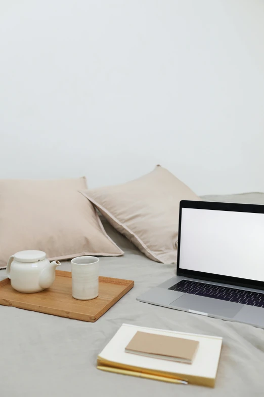 a laptop computer sitting on top of a bed, trending on pexels, light beige pillows, table in front with a cup, plain background, developers