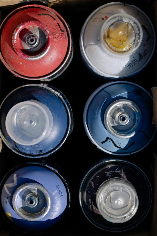 a box filled with lots of different colored cans, an airbrush painting, by Doug Ohlson, close up shots, 6 colors, black paint, blue and white and red mist