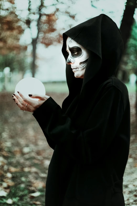 a person dressed as a skeleton holding a white ball, pexels contest winner, dressed in a black cloak, ((skull)), wearing a black hoodie, wiccan