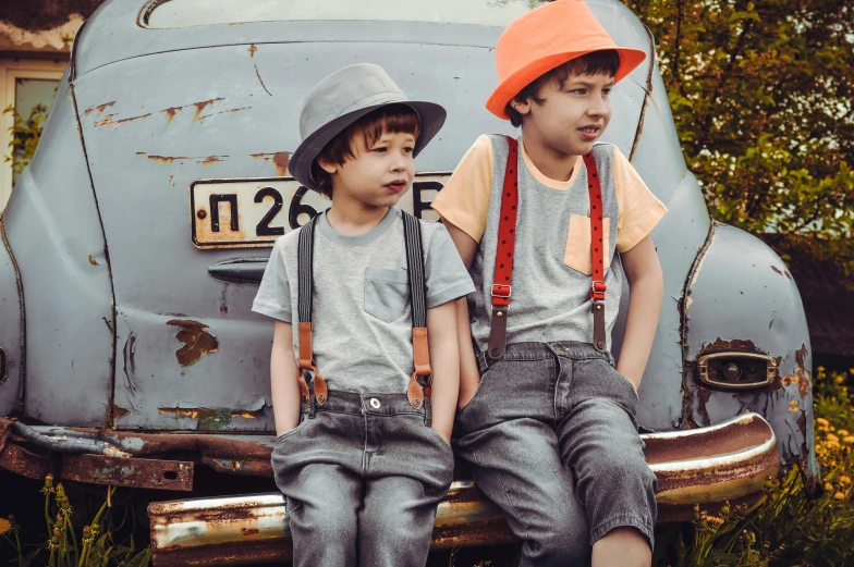 two young boys sitting on the back of a car, by Lucia Peka, pexels, hats, grey orange, suspenders, vintage theme
