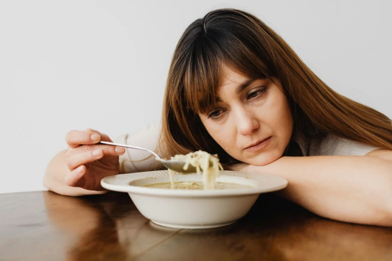 a woman sitting at a table with a bowl of food, trending on pexels, very sad face, good soup, square, high quality photo