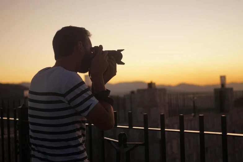 a man taking a picture with a camera, a picture, by Alexis Grimou, sunset evening lighting, shot from roofline, athens in the background, profile pose