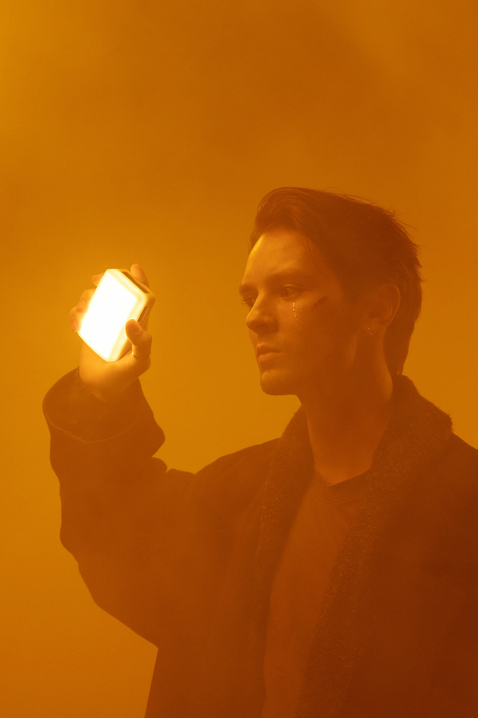 a man holding a cell phone up in the air, by Jonas De Ro, bauhaus, glowing amber, glowing powder, benedict cumberbatch, ignant