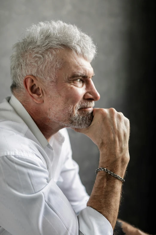 a man that is sitting down with his hand on his chin, by László Beszédes, pexels contest winner, photorealism, silver hair and beard, wearing a white shirt, philippe starck, looking serious