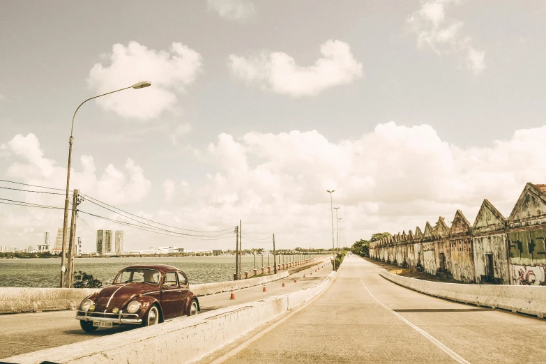 a car that is sitting on the side of a road, a colorized photo, pexels contest winner, tropical coastal city, old bridge, wes anderson background, beetle