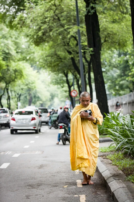 a man in a yellow robe walking down a street, inspired by Steve McCurry, happening, checking her phone, hoang lap, park, wearing jedi robes and a sari