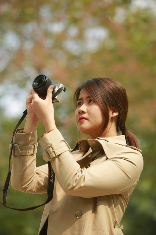 a woman taking a picture with a camera, by Basuki Abdullah, woman is in a trenchcoat, in an action pose, headshot profile picture, vietnamese woman