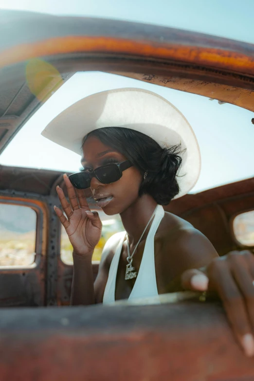 a woman sitting in the driver's seat of an old car, trending on pexels, afrofuturism, white cowboy hat, sunfaded, adut akech, palm springs