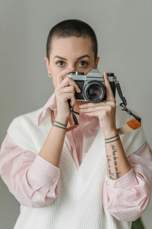 a woman taking a picture with a camera, posing for the camera, facing the camera, looking down on the camera, body and headshot